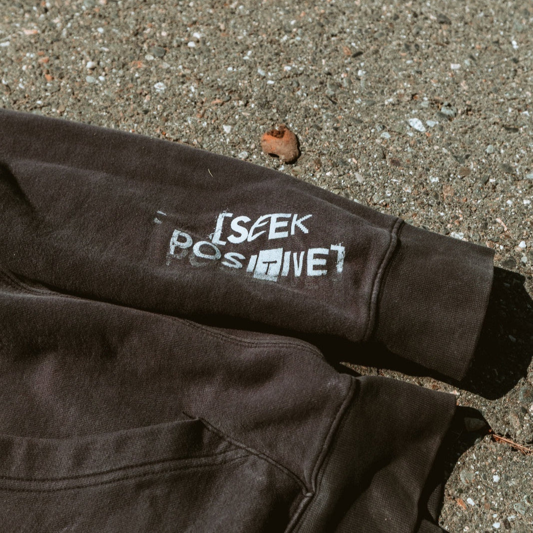 Brown jacket with 'I seek positive' text on a concrete surface